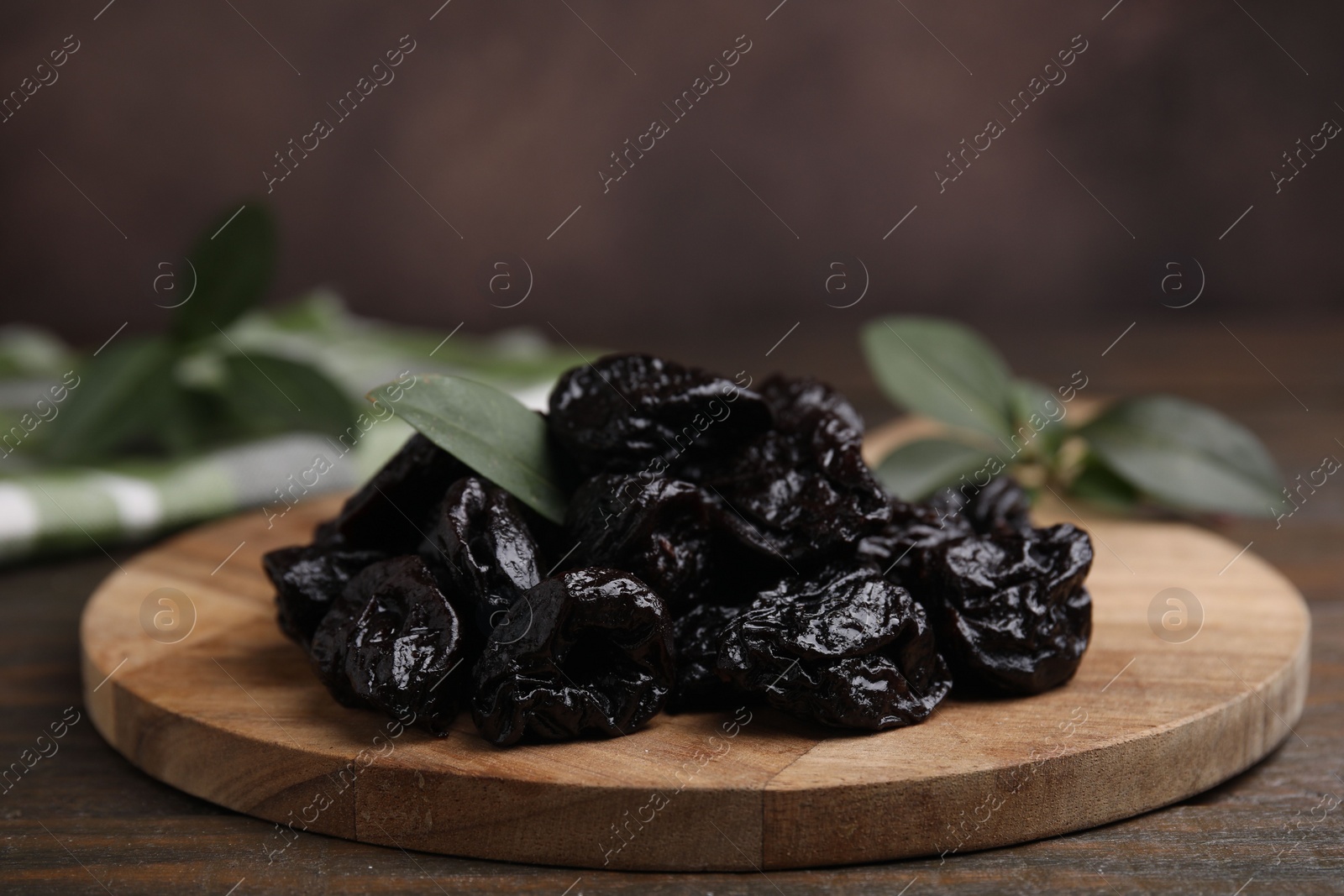 Photo of Tasty dried prunes and green leaf on wooden table, closeup. Space for text