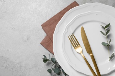 Stylish setting with cutlery and eucalyptus leaves on light grey table, flat lay. Space for text