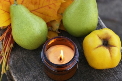Photo of Burning candle, tasty fruits and beautiful dry leaves on wooden surface, above view. Autumn atmosphere