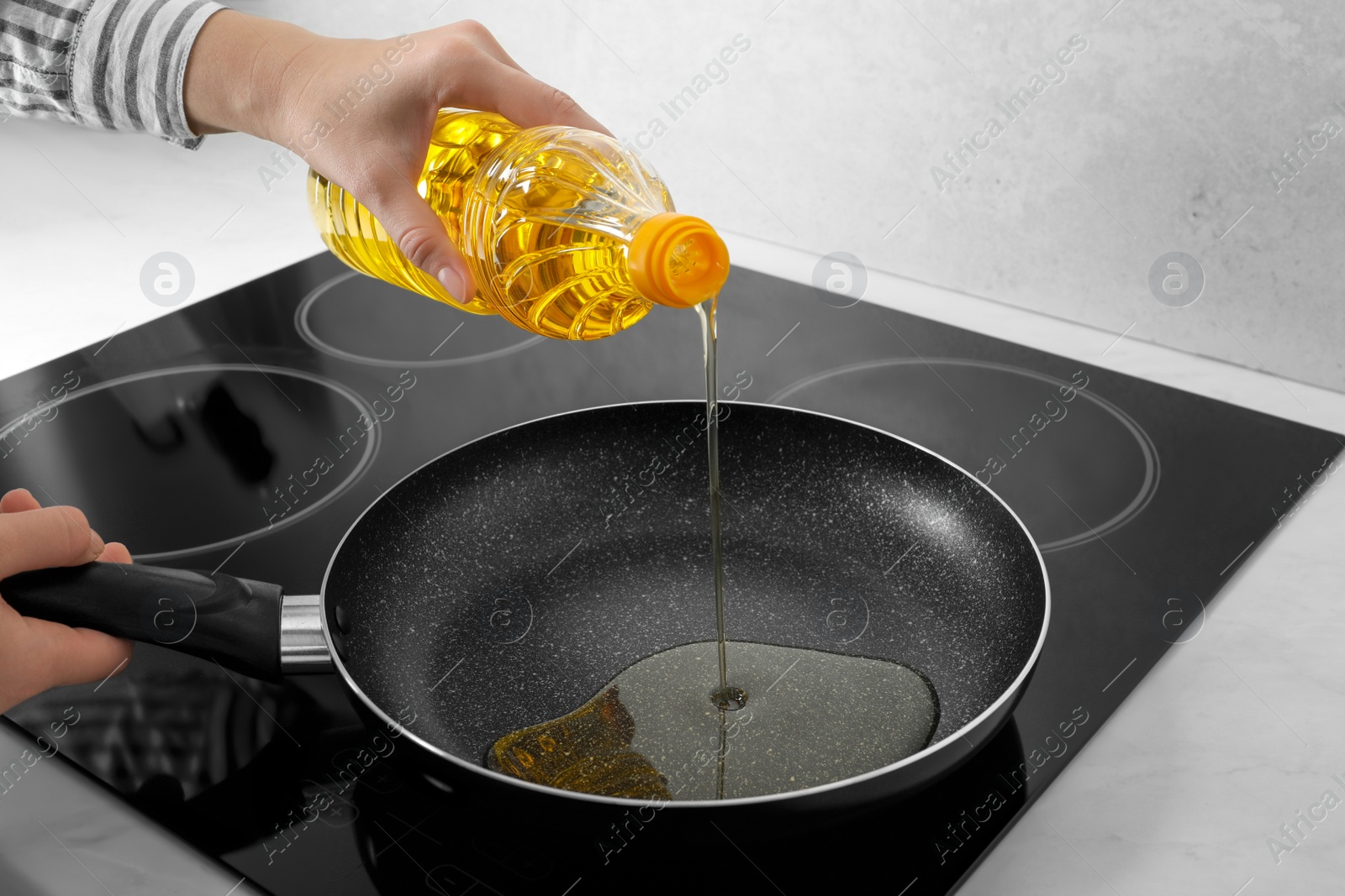 Photo of Woman pouring cooking oil from bottle into frying pan on stove, closeup