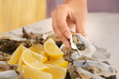 Woman holding fresh oyster over plate, focus on hand