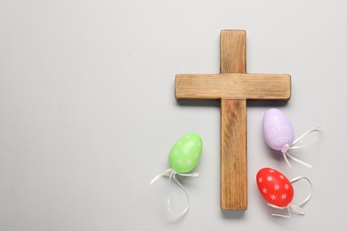 Wooden cross and painted Easter eggs on light grey background, flat lay. Space for text