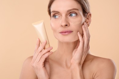 Woman holding tube of foundation on beige background