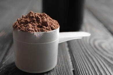 Photo of Scoop of chocolate protein powder on black wooden table