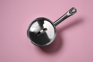 Steel saucepan with lid on pink background, top view