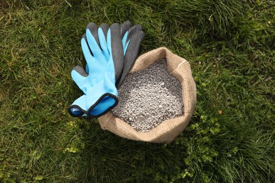 Photo of Fertilizer in bag and gloves on green grass outdoors, flat lay