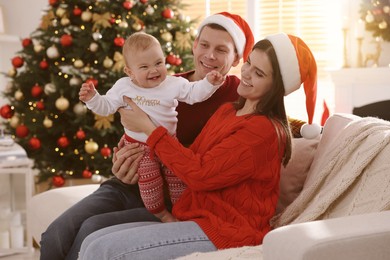 Happy couple with cute baby on sofa in room decorated for Christmas