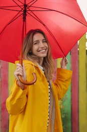 Photo of Beautiful young woman in stylish autumn clothes with red umbrella near color fence