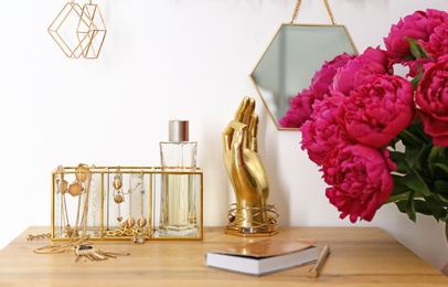 Composition with gold accessories and flowers on dressing table near white wall