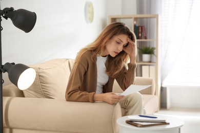 Photo of Worried woman reading letter on sofa at home