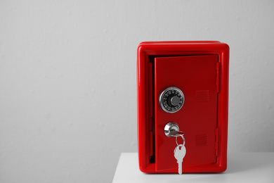 Photo of Red steel safe with keys on table against light wall. Space for text
