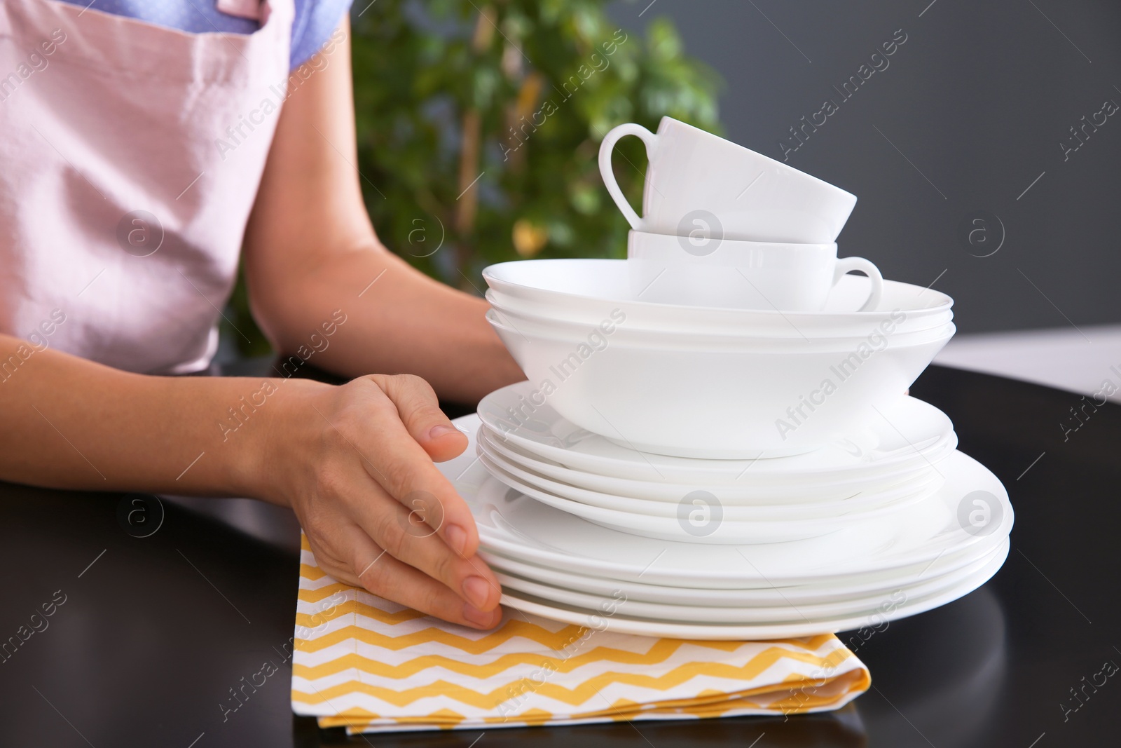 Photo of Woman with clean dishes on table in kitchen, closeup