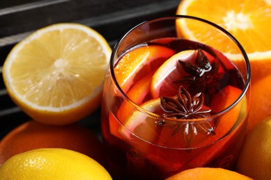 Photo of Glass of aromatic punch drink and fresh citrus fruits on table, closeup
