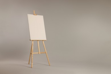 Wooden easel with blank canvas on grey background. Space for text