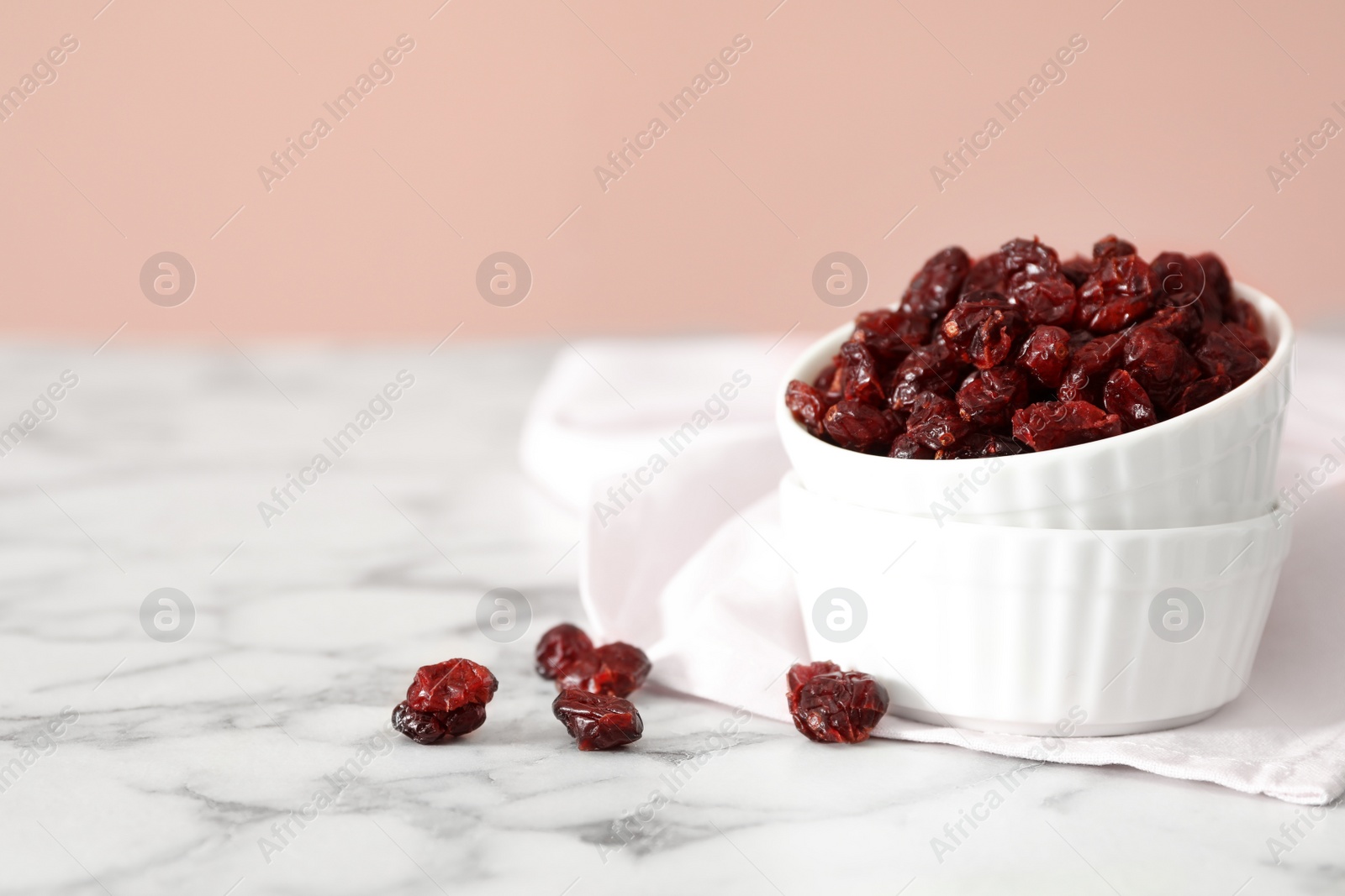 Photo of Dried cranberries in bowl on white marble table, space for text