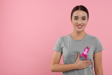 Photo of Beautiful young woman with pink ribbon on color background, space for text. Breast cancer awareness