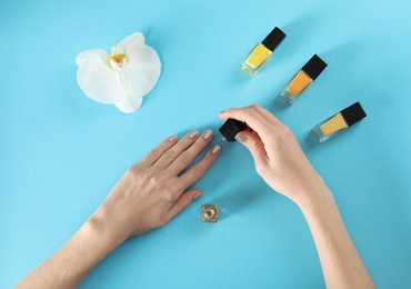 Woman applying nail polish on color background, top view