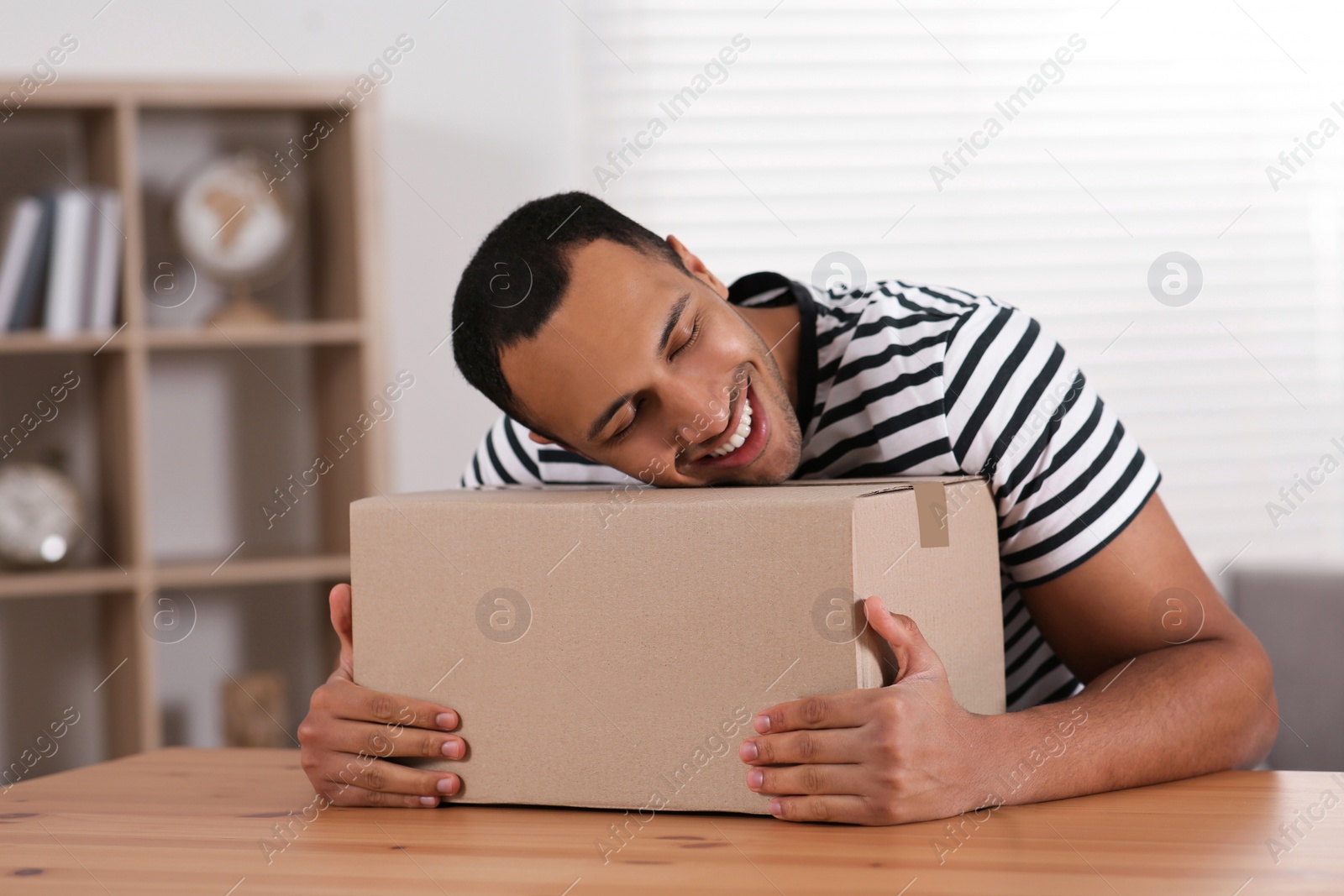 Photo of Happy young man with parcel at table indoors. Internet shopping