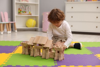 Little boy playing with wooden entry gate on puzzle mat in room. Child's toy