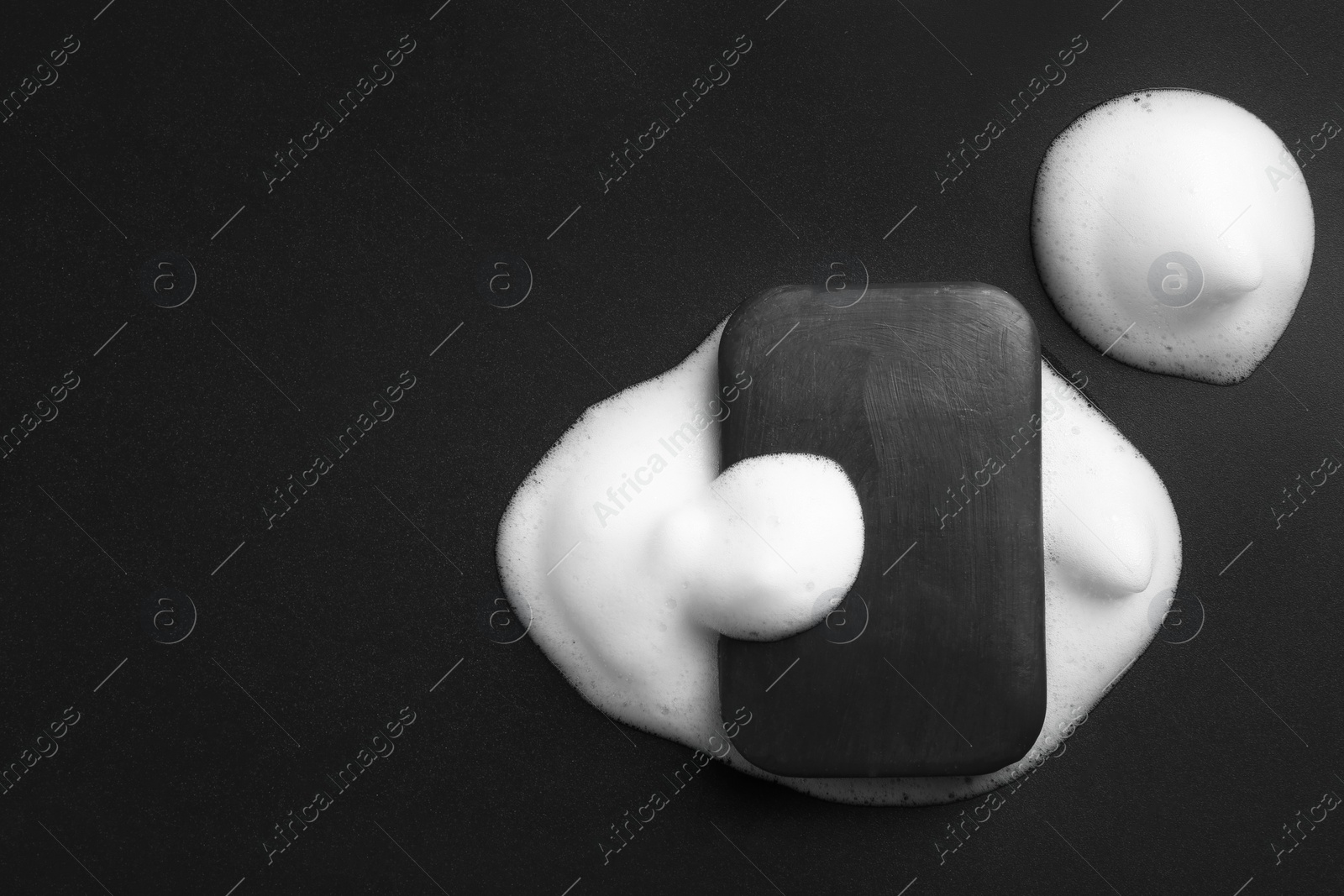 Photo of Soap bar and foam on black background, top view. Space for text