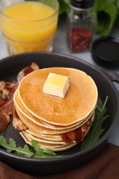 Photo of Tasty pancakes with butter, fried bacon and fresh arugula on grey table