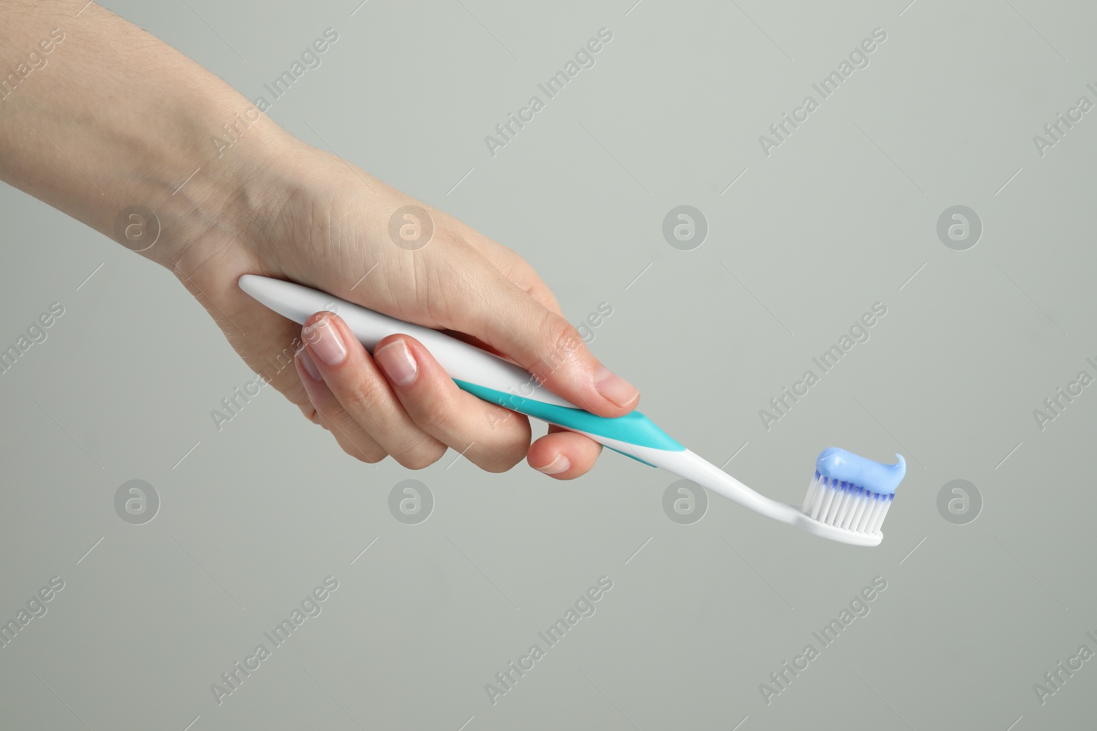 Photo of Woman holding toothbrush with paste on light grey background, closeup