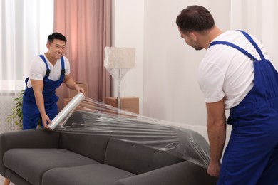 Workers wrapping sofa in stretch film indoors