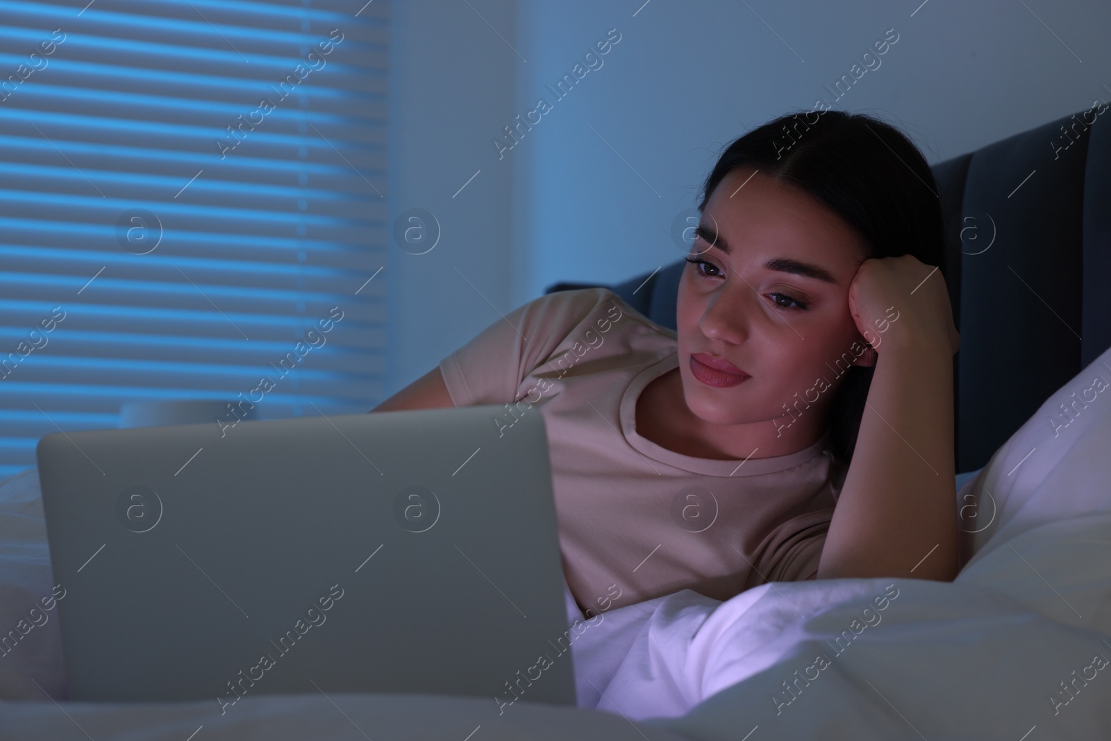 Photo of Young woman using laptop in bed at night. Internet addiction