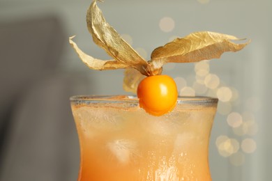 Photo of Refreshing cocktail decorated with physalis fruit against blurred festive lights, closeup