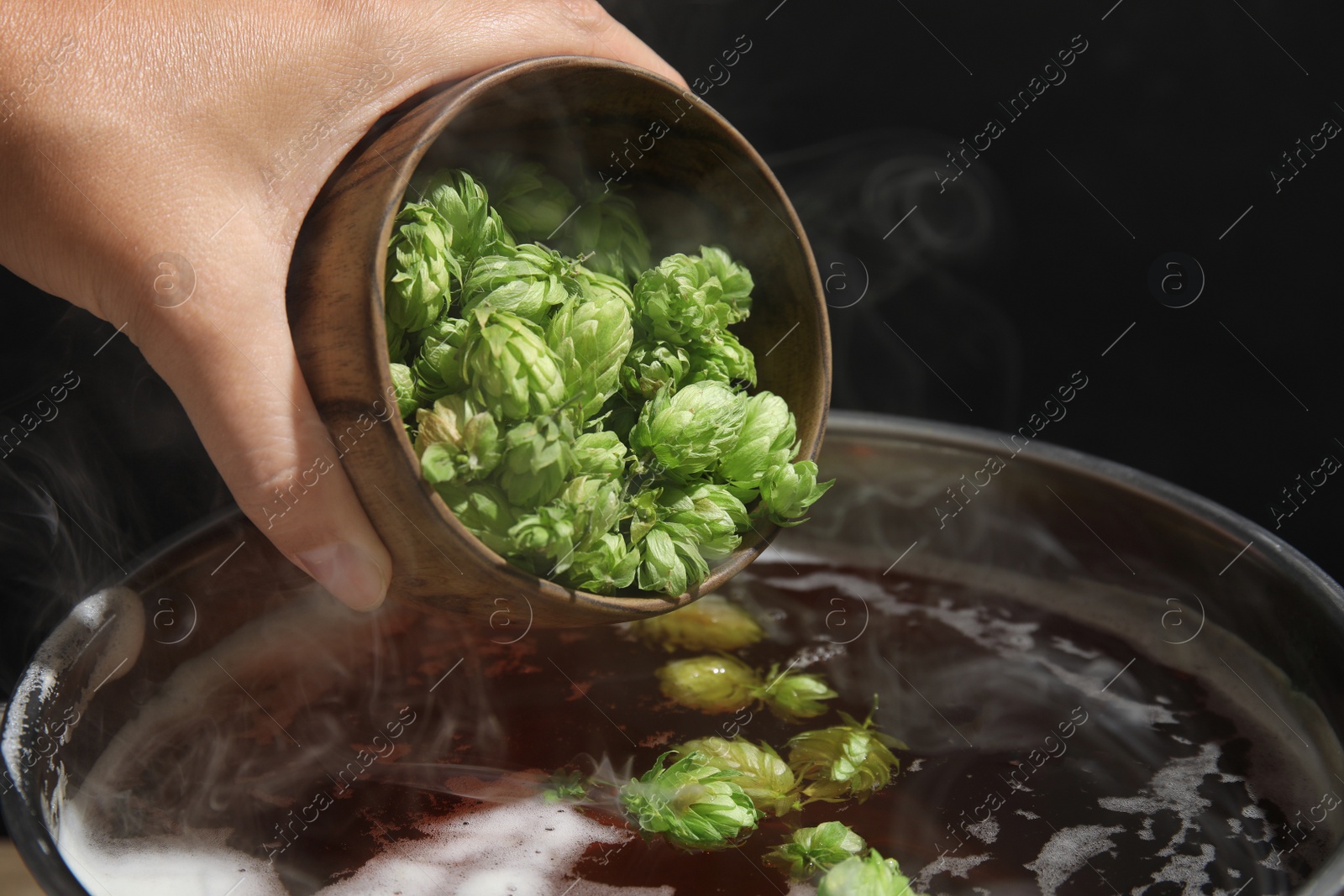 Photo of Woman adding fresh green hops to beer wort in pot, closeup