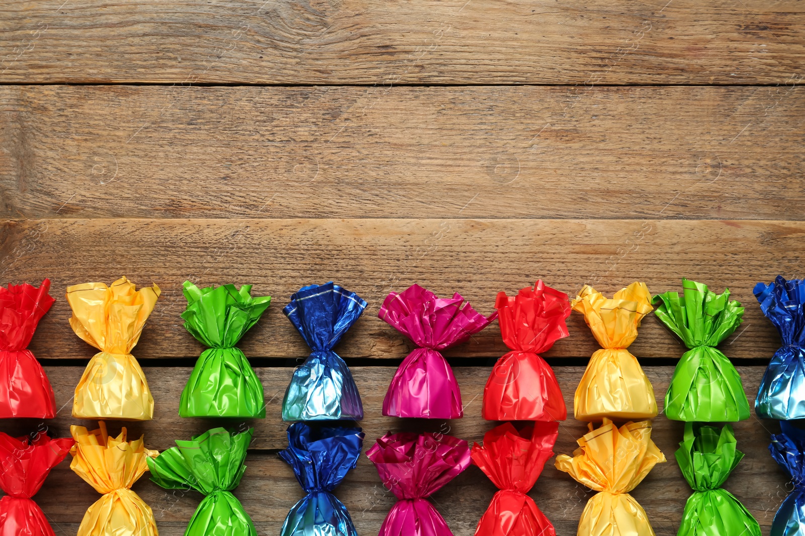 Photo of Candies in colorful wrappers on wooden table, flat lay. Space for text