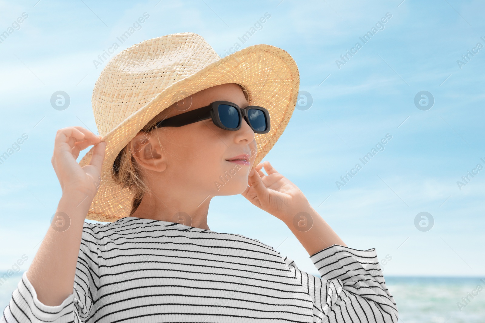 Photo of Little girl wearing sunglasses and hat at beach on sunny day