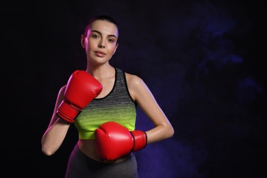 Photo of Portrait of beautiful woman wearing boxing gloves in color lights on black background. Space for text