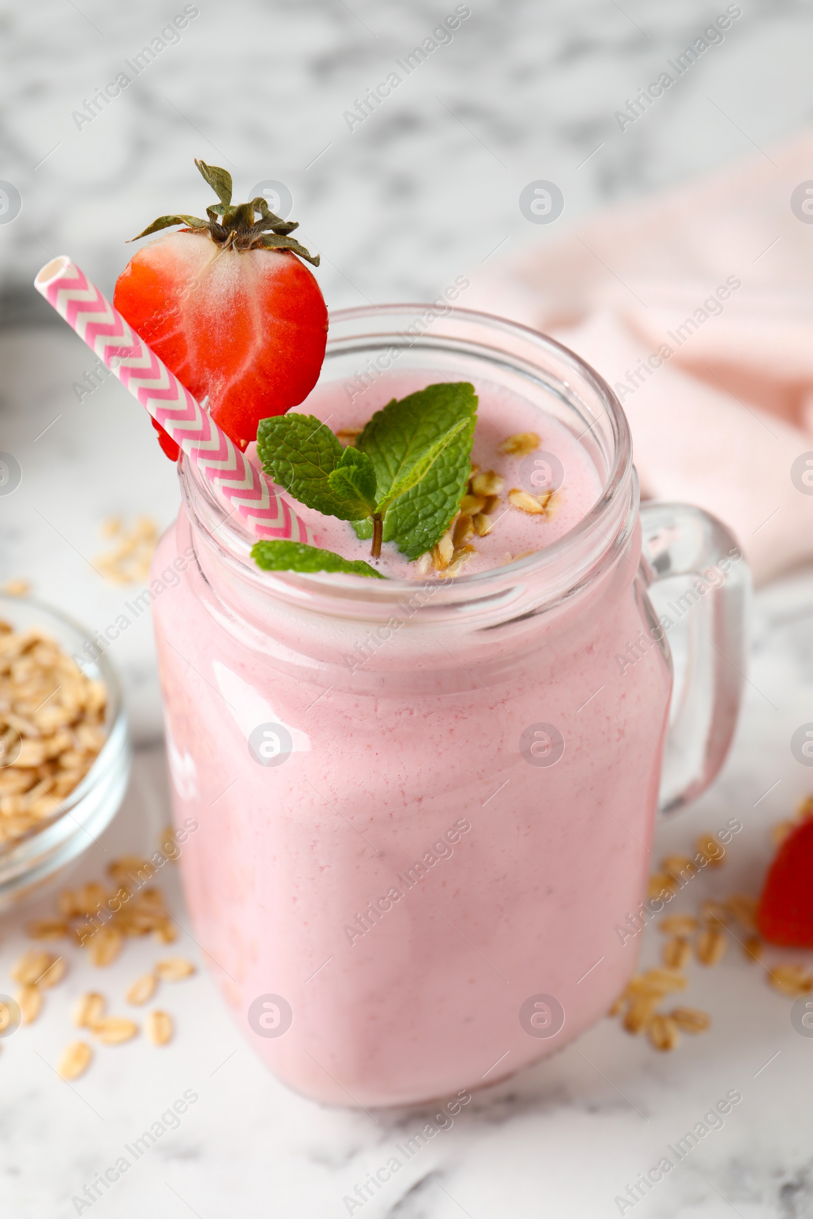 Photo of Mason jar of tasty strawberry smoothie with oatmeal and mint on white marble table