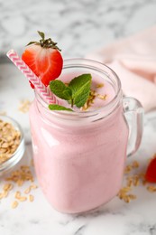 Photo of Mason jar of tasty strawberry smoothie with oatmeal and mint on white marble table