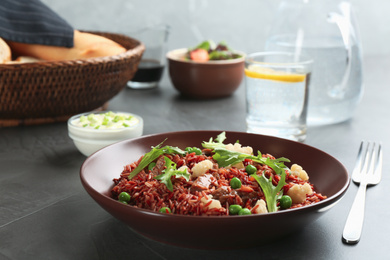 Photo of Tasty brown rice with meat and vegetables served on dark grey table