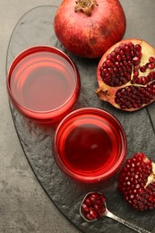 Photo of Tasty pomegranate juice in glasses and fresh fruit on grey table, top view