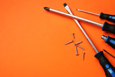 Photo of Set of screwdrivers and screws on orange background, flat lay. Space for text