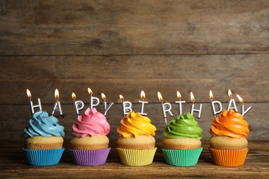 Photo of Birthday cupcakes with burning candles on table against wooden background. Space for text