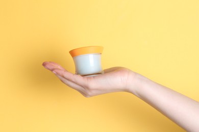 Photo of Woman holding jar of cream on yellow background, closeup