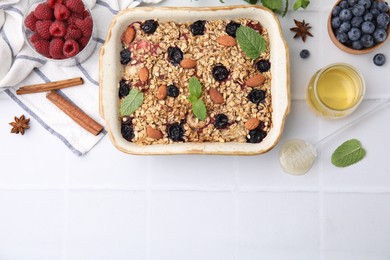 Photo of Tasty baked oatmeal with berries, almonds and spices in baking tray on white tiled table, flat lay. Space for text