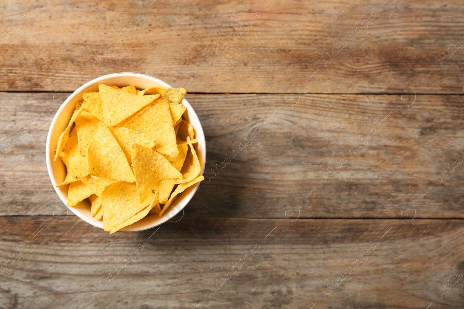 Photo of Tasty mexican nachos chips in bowl on wooden table, top view. Space for text