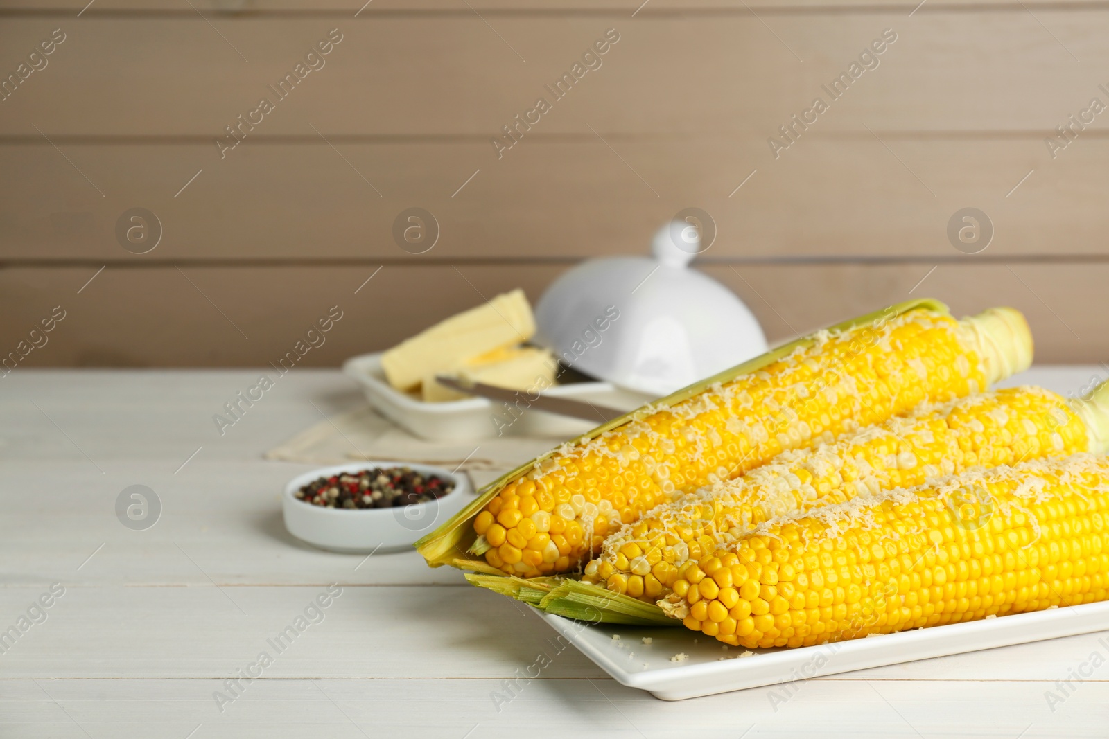 Photo of Plate with tasty cooked corn cobs on white wooden table, space for text
