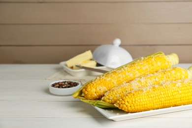 Plate with tasty cooked corn cobs on white wooden table, space for text