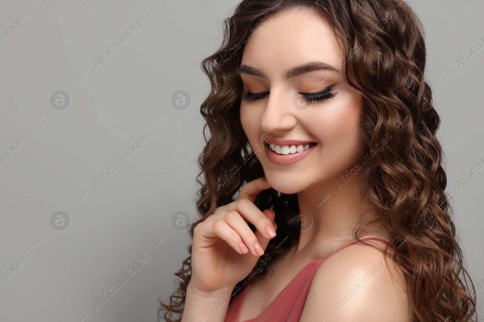 Photo of Beautiful young woman with long curly brown hair on grey background, space for text