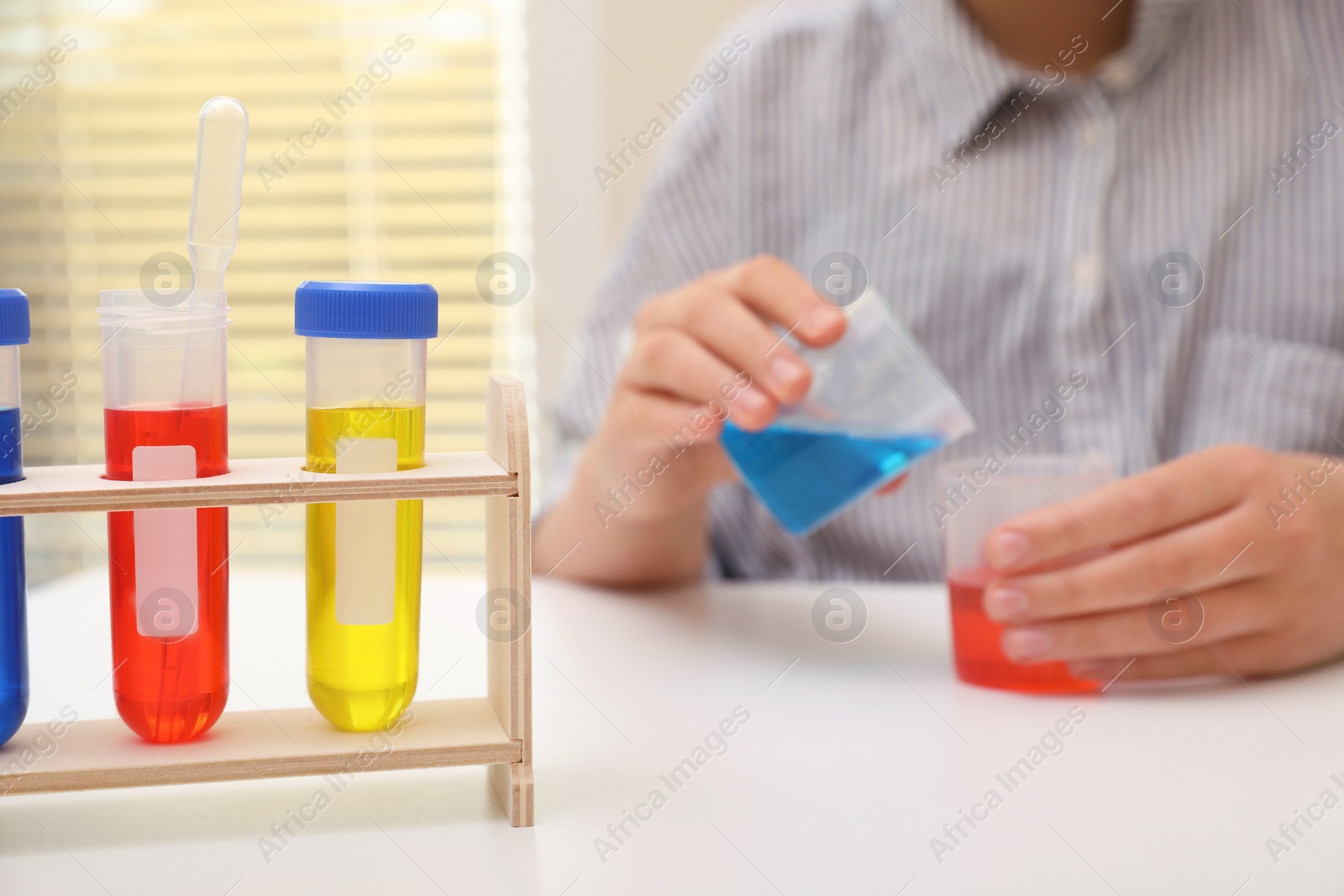 Photo of Girl mixing colorful liquids at white table indoors, selective focus. Kids chemical experiment set