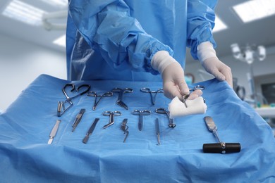 Image of Nurse near table with different surgical instruments in operating room, closeup