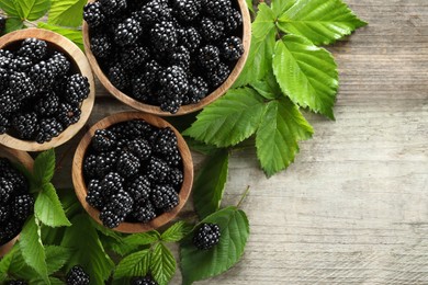 Photo of Ripe blackberries and green leaves on wooden table, flat lay. Space for text