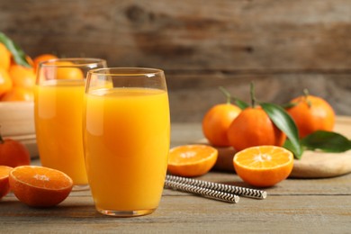 Photo of Glasses of fresh tangerine juice and fruits on wooden table. Space for text