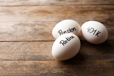 Photo of Eggs with words PENSION, RETIRE and 401k on wooden background. Space for text